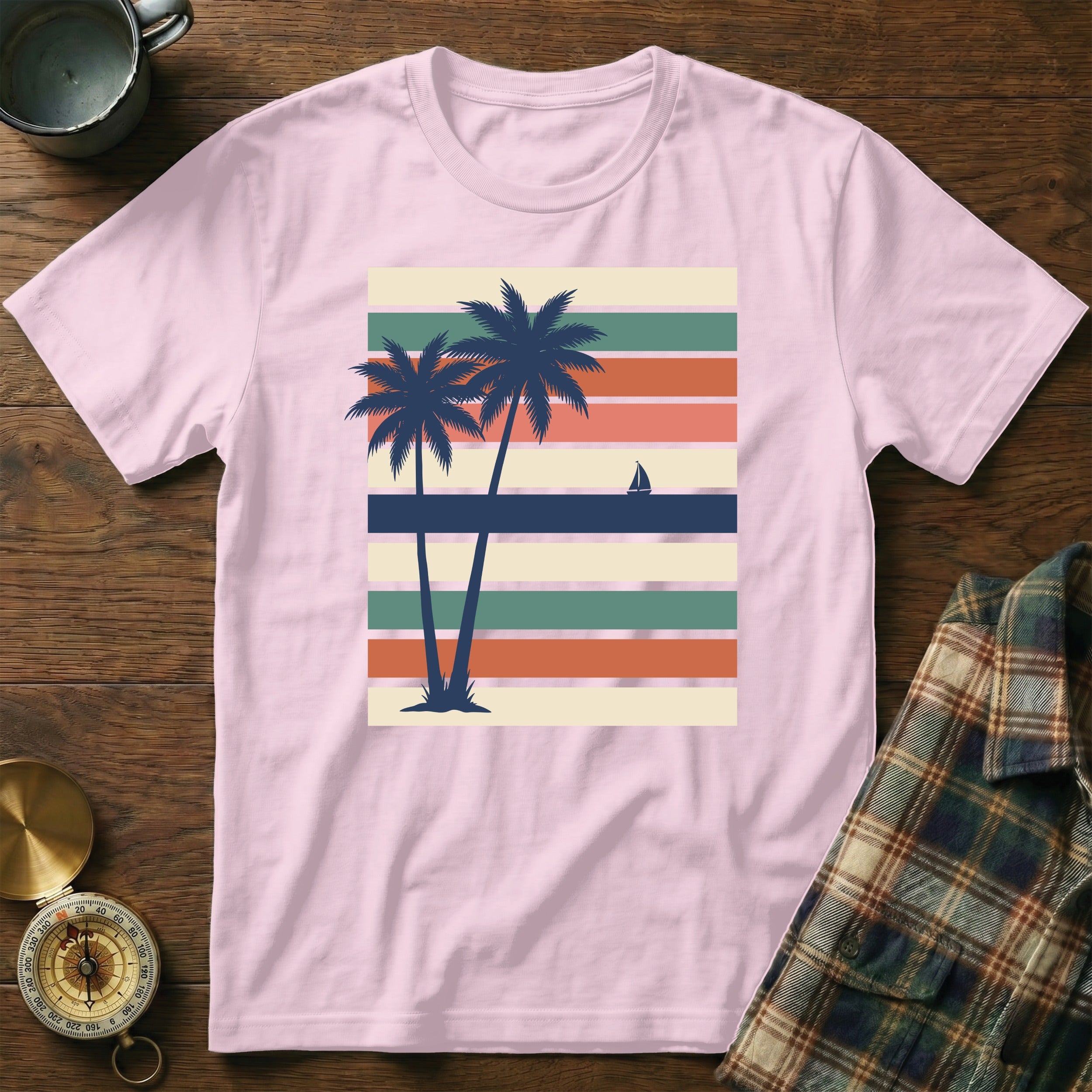 Pink t-shirt with two palm trees and a sailboat on striped background.