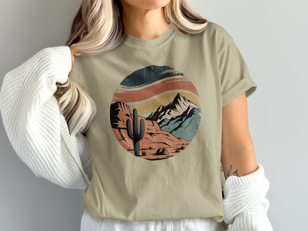 Circular desert landscape graphic with cactus and mountains on tan t-shirt.