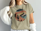 Circular desert landscape graphic with cactus and mountains on tan t-shirt.
