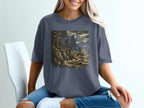 Graphic t-shirt with Bigfoot silhouette on rocky coast overlooking ocean at night.