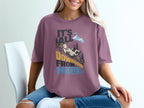 A woman wearing a mauve t-shirt with a graphic of a goat sliding down a mountain and the text it's all downhill from here.