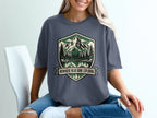 Dark gray t-shirt with shield logo featuring mountains, trees, reflection, and text.