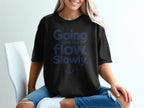 A woman wearing a black t-shirt with blue text that reads Going with the flow. Slowly. and an anchor graphic.