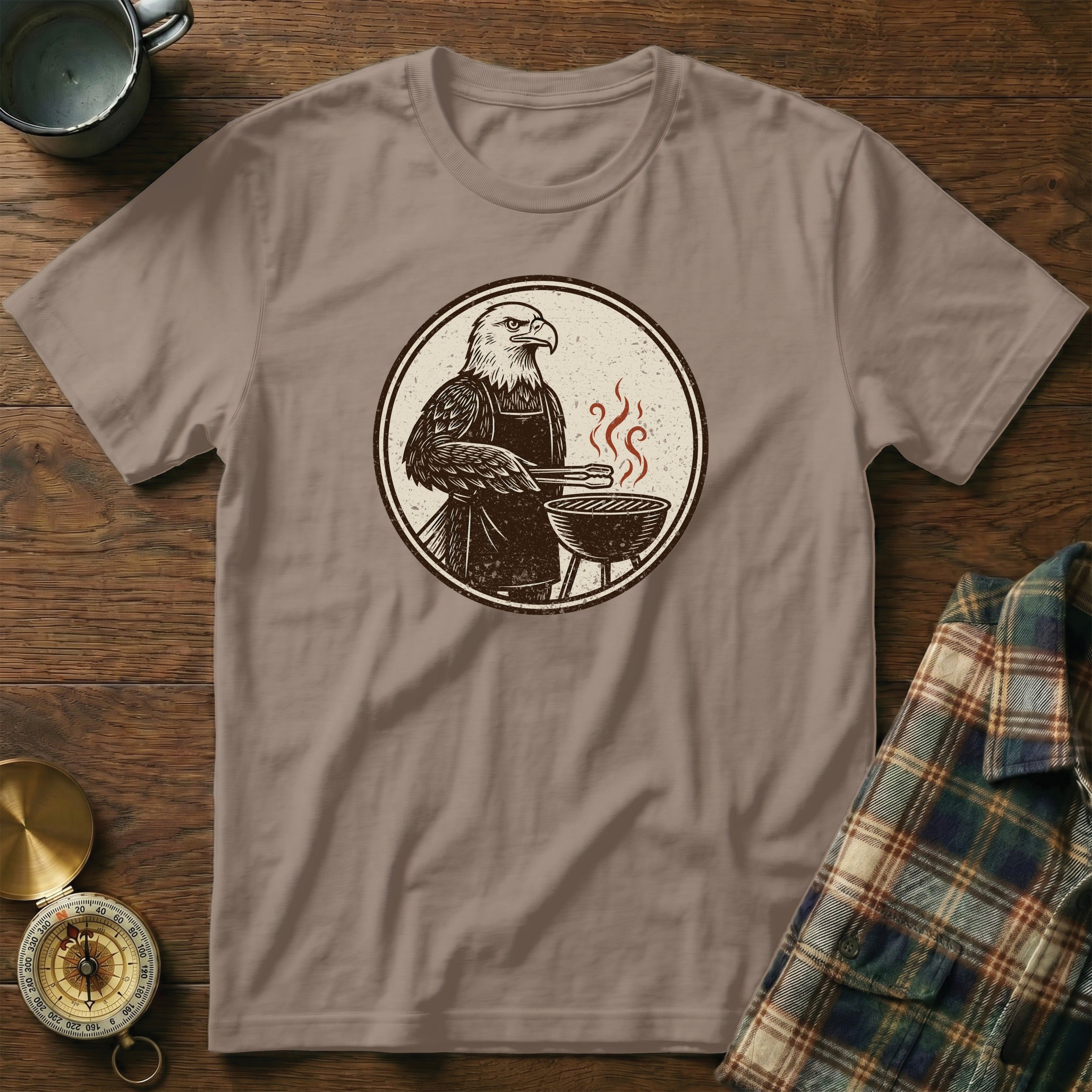 Graphic tee with an eagle wearing an apron grilling on a barbecue.