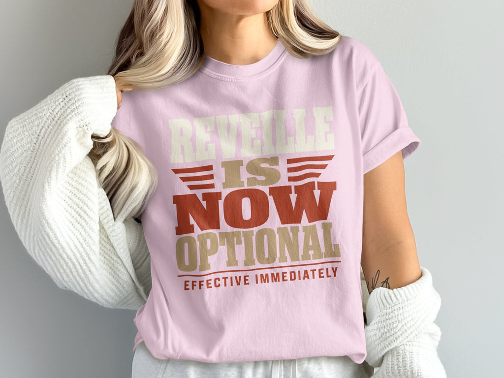 A person wears a light pink t-shirt with the text "REVEILLE IS NOW OPTIONAL EFFECTIVE IMMEDIATELY".