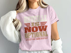 A person wears a light pink t-shirt with the text "REVEILLE IS NOW OPTIONAL EFFECTIVE IMMEDIATELY".