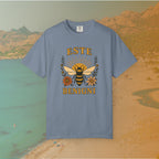 blue t-shirt Vintage-style graphic tee featuring a large, central honey bee with sunburst wings, flanked by retro flowers. The Latin words "ESTE BENIGNI" for "BEE KIND" are printed above and below the design.