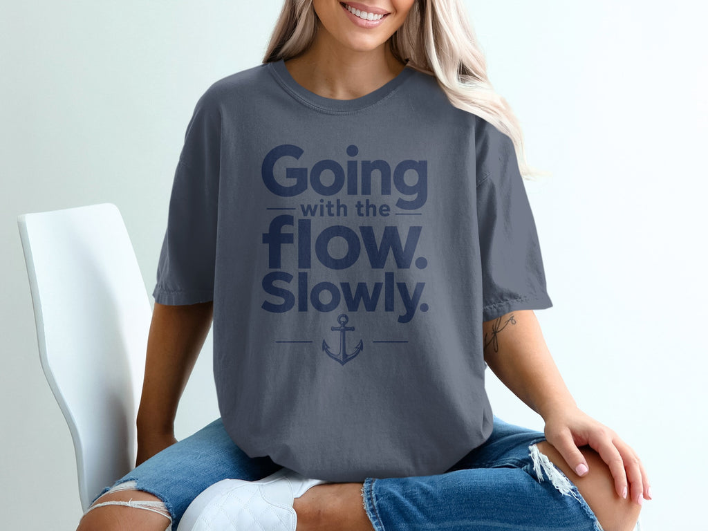 A blonde woman sitting on a white chair wears a dark gray t-shirt with blue text reading Going with the flow. Slowly. and an anchor graphic.