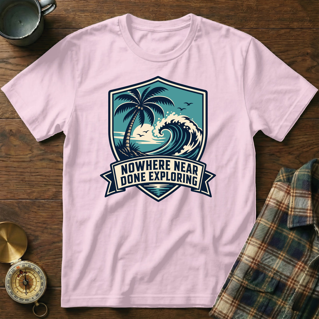 Pink t-shirt with a shield graphic of a palm tree, wave, and sun text "NOWHERE NEAR DONE EXPLORING".
