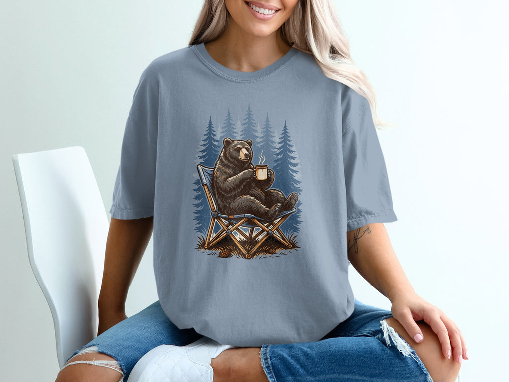 Bear sitting in a chair holding a coffee mug with pine trees in the background.