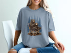 Bear sitting in a chair holding a coffee mug with pine trees in the background.