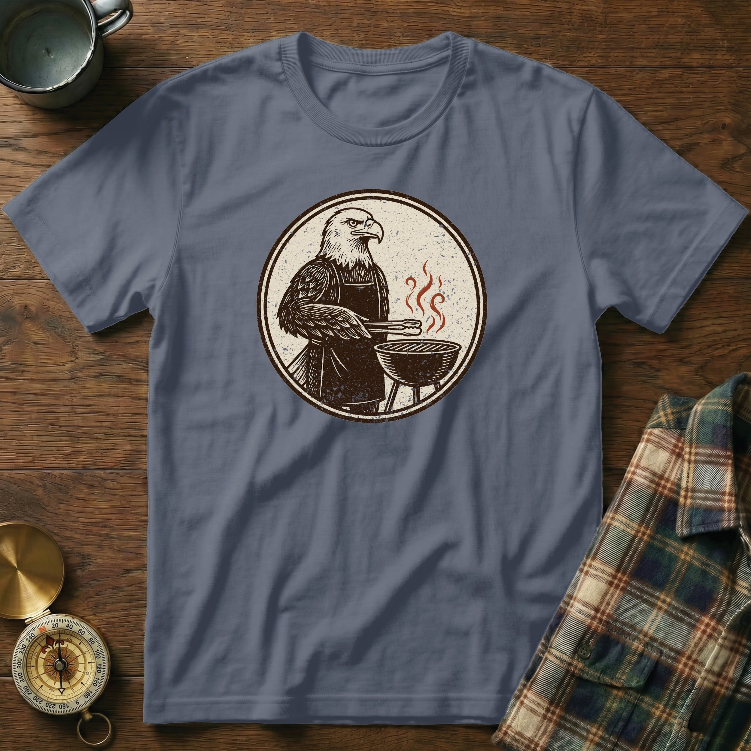 Eagle wearing an apron grilling with tongs and a barbecue on a t-shirt.