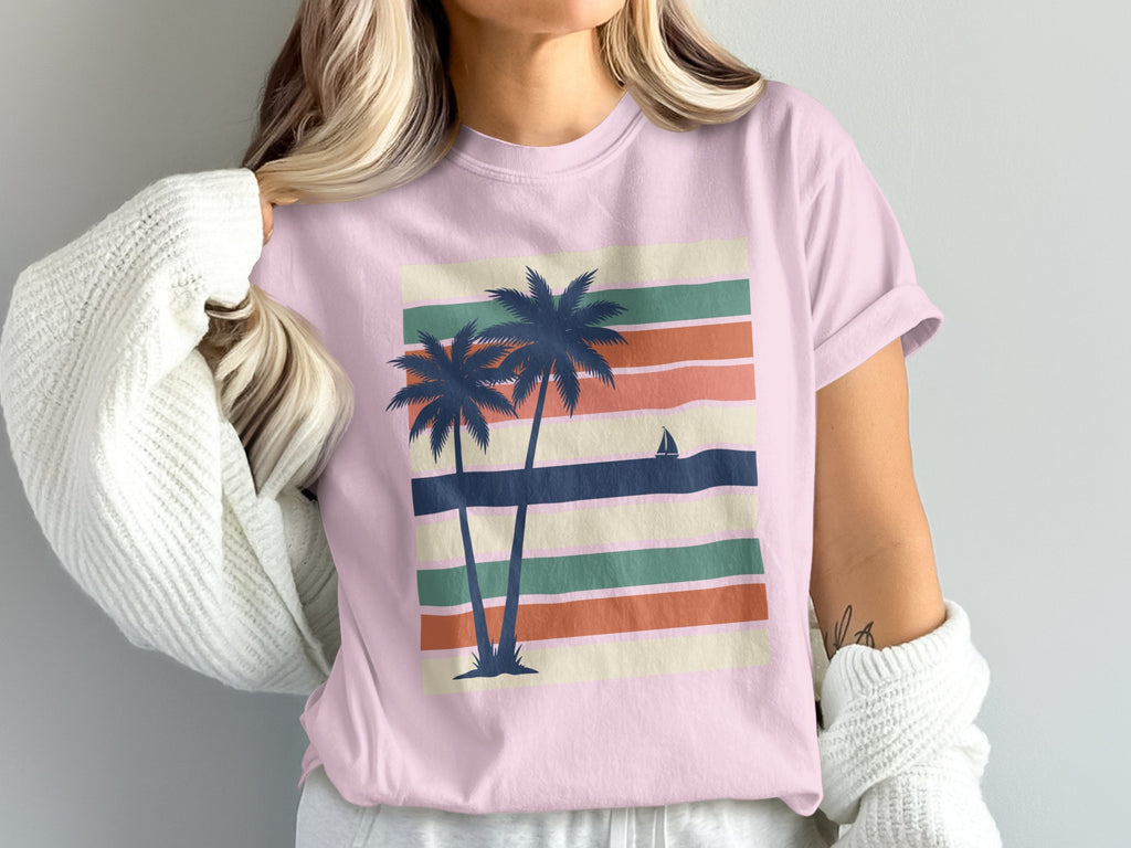 Pink t-shirt with palm trees and sailboat on striped background.