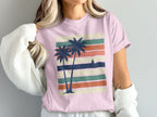 Pink t-shirt with palm trees and sailboat on striped background.
