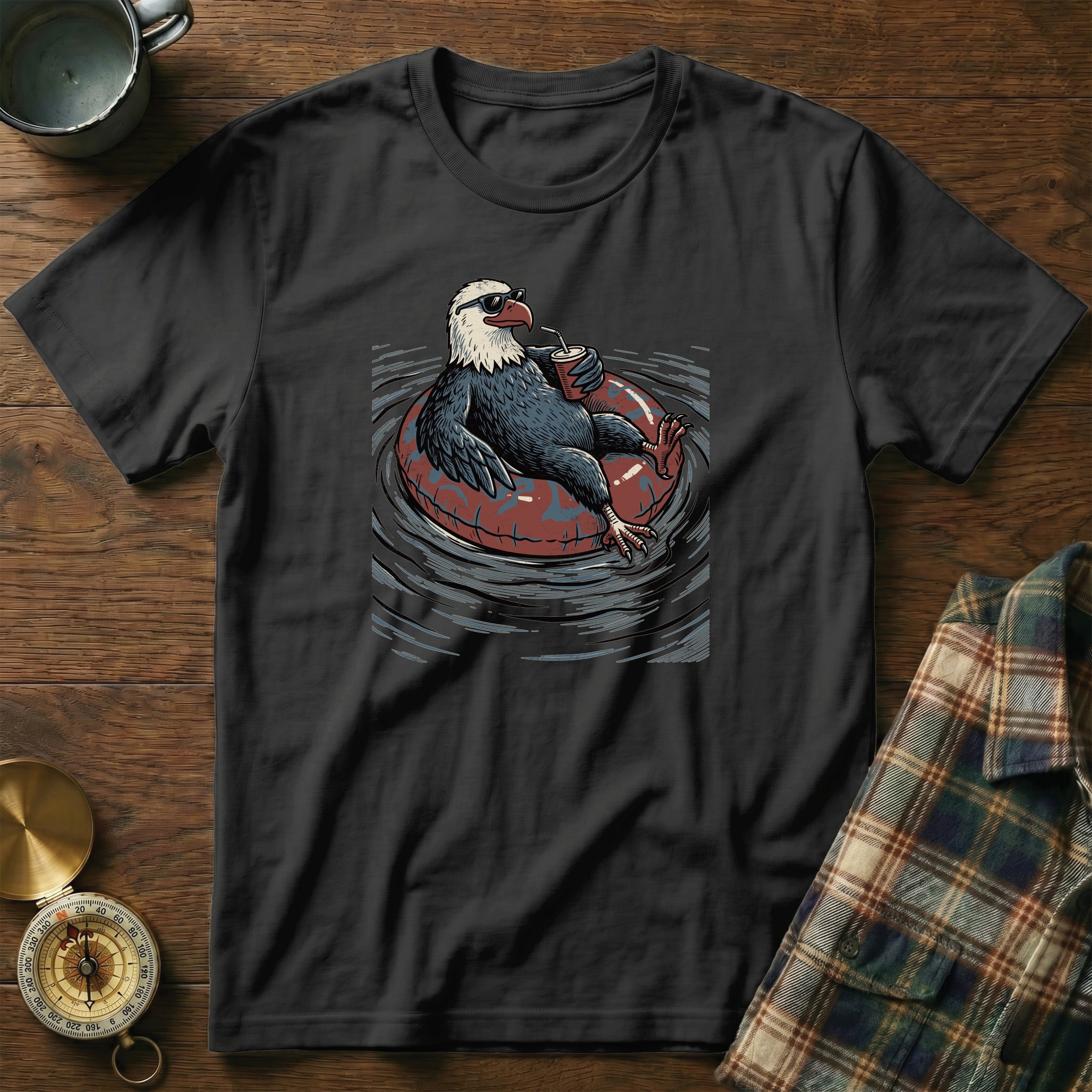 Black t-shirt with a graphic of an eagle wearing sunglasses relaxing on an inner tube with a drink.