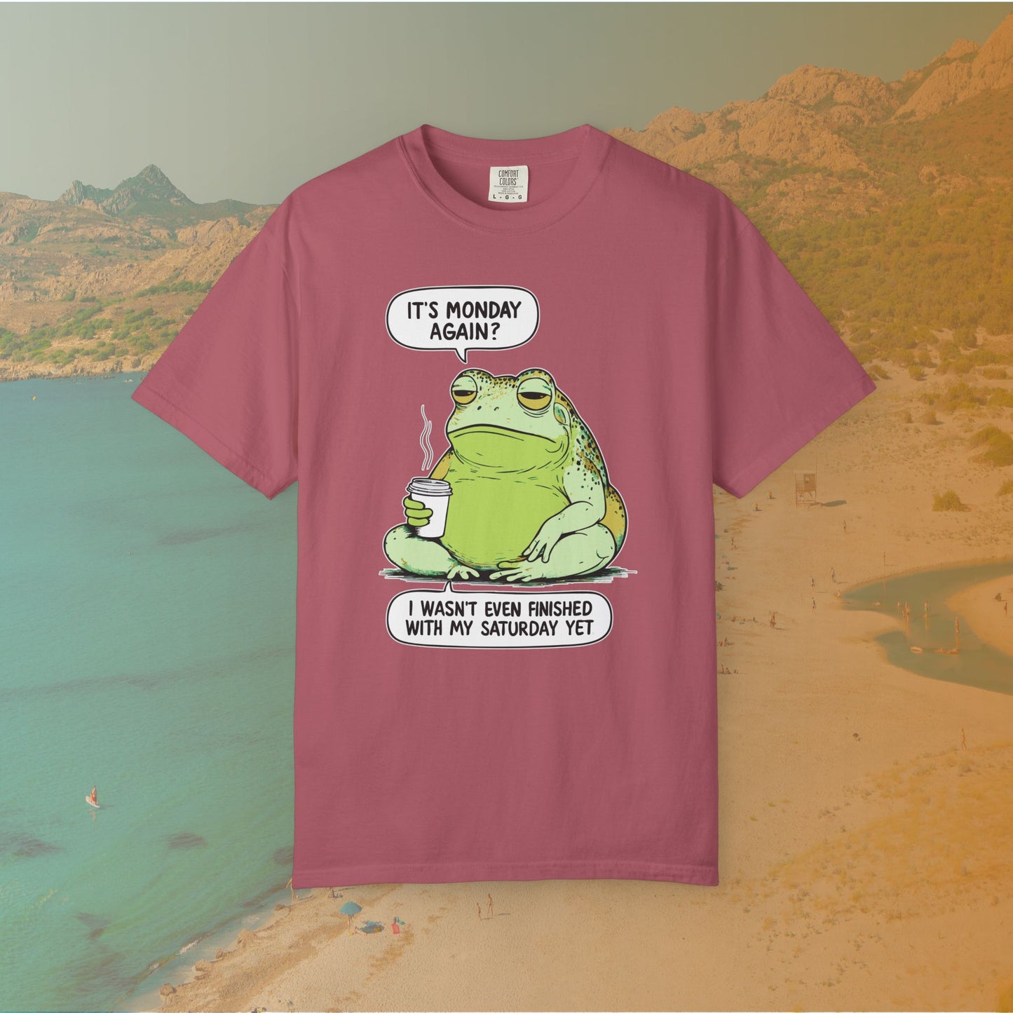 maroon t-shirt Funny T-shirt graphic featuring a large, grumpy toad holding a to-go coffee cup. The cartoon is captioned with the quotes: "IT'S MONDAY AGAIN? I WASN'T EVEN FINISHED WITH MY SATURDAY YET.