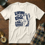 White t-shirt with navy graphic of goat hanging from cliff, text "LIVING ON THE EDGE, BARELY."