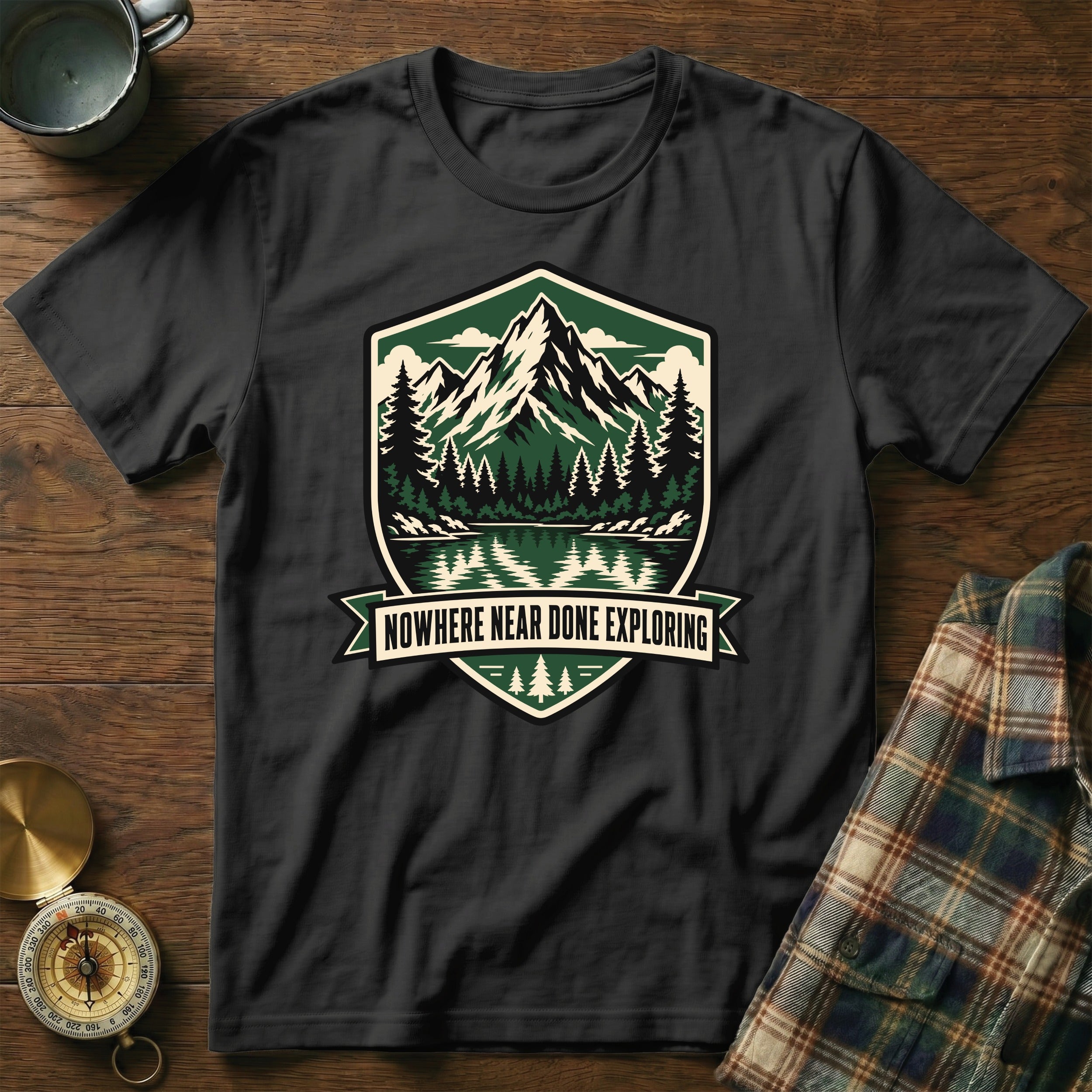 Black t-shirt with mountain, lake, and forest emblem that reads "NOWHERE NEAR DONE EXPLORING".