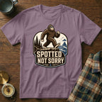 T-shirt with Bigfoot graphic and text "Spotted Not Sorry" on a rustic wooden background.