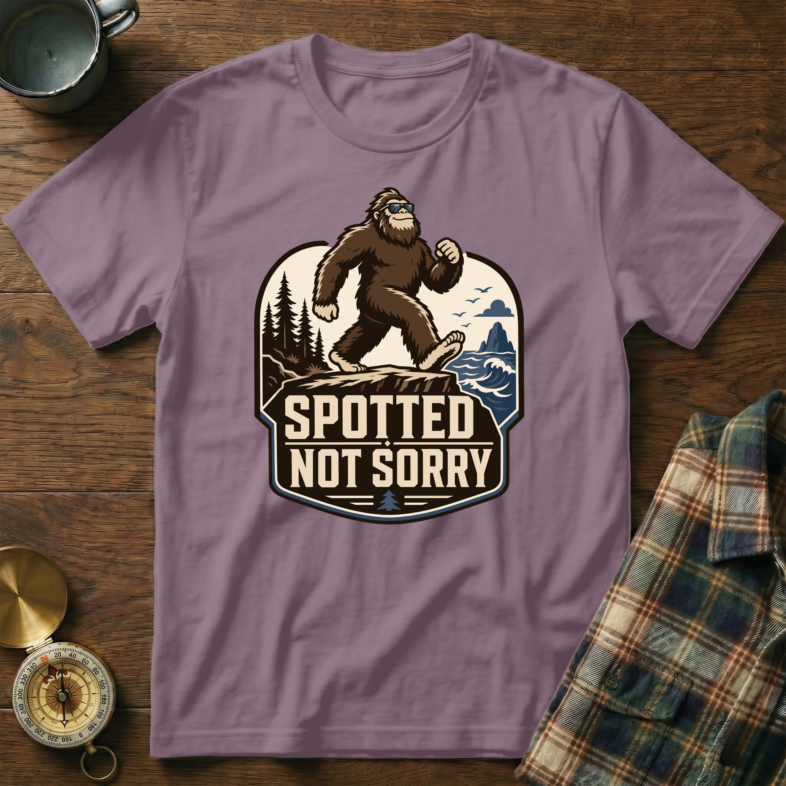 T-shirt with Bigfoot graphic and text "Spotted Not Sorry" on a rustic wooden background.