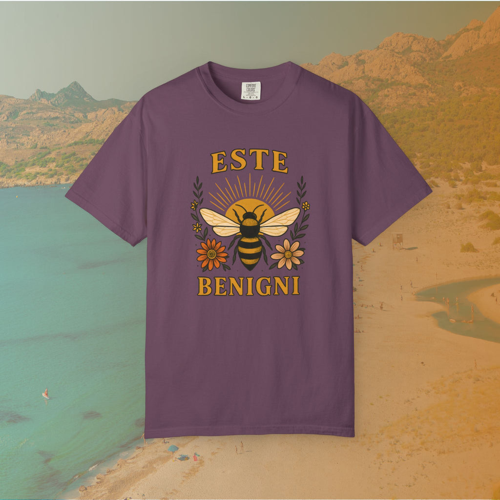 purple t-shirt Vintage-style graphic tee featuring a large, central honey bee with sunburst wings, flanked by retro flowers. The Latin words "ESTE BENIGNI" for "BEE KIND" are printed above and below the design.
