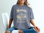 A person wearing a grey t-shirt featuring a mountain graphic and the text Mountain Sunrise hike. Sunset arrival.