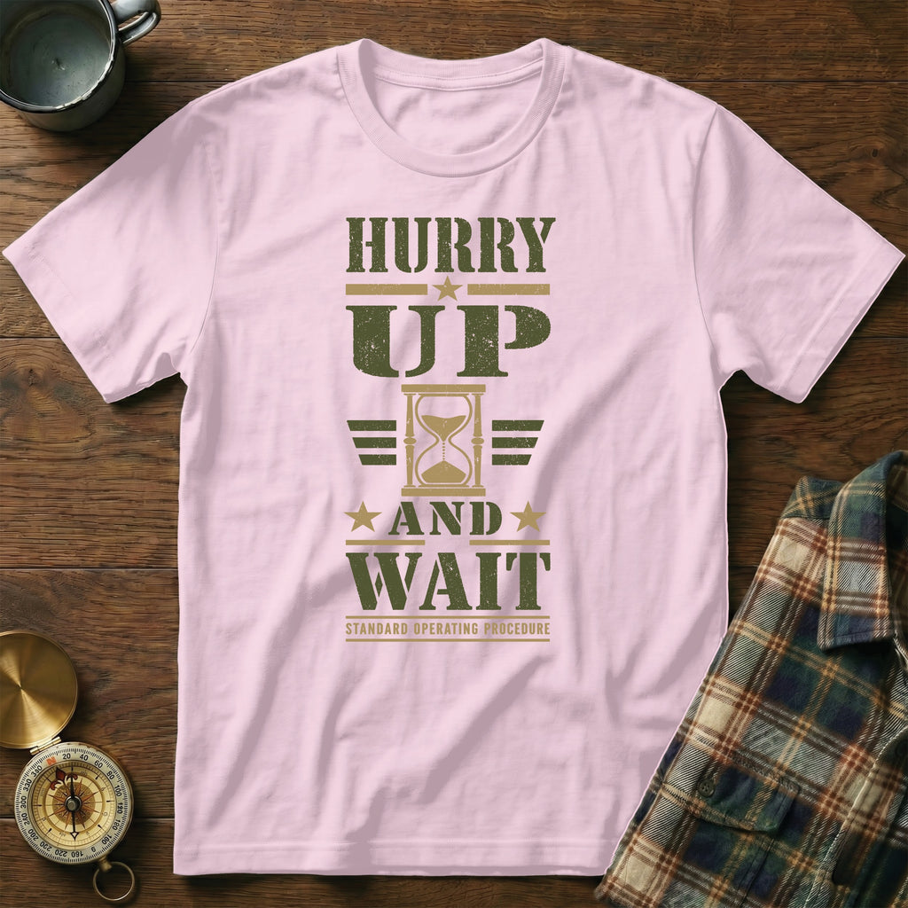 A light pink t-shirt with olive green text reading "Hurry Up and Wait" and an hourglass graphic.