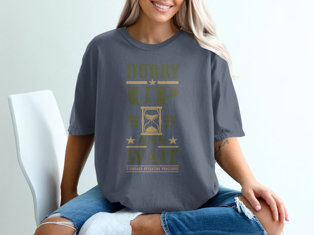 A person wearing a grey t-shirt featuring the text "Hurry Up And Wait Standard Operating Procedure" with an hourglass graphic.