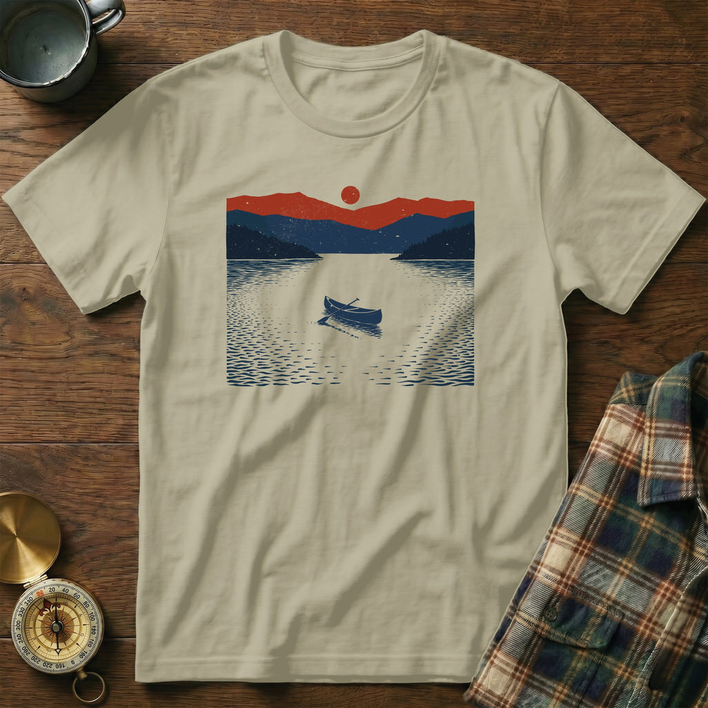 T-shirt with a graphic of a canoe on a lake at sunset with mountains.