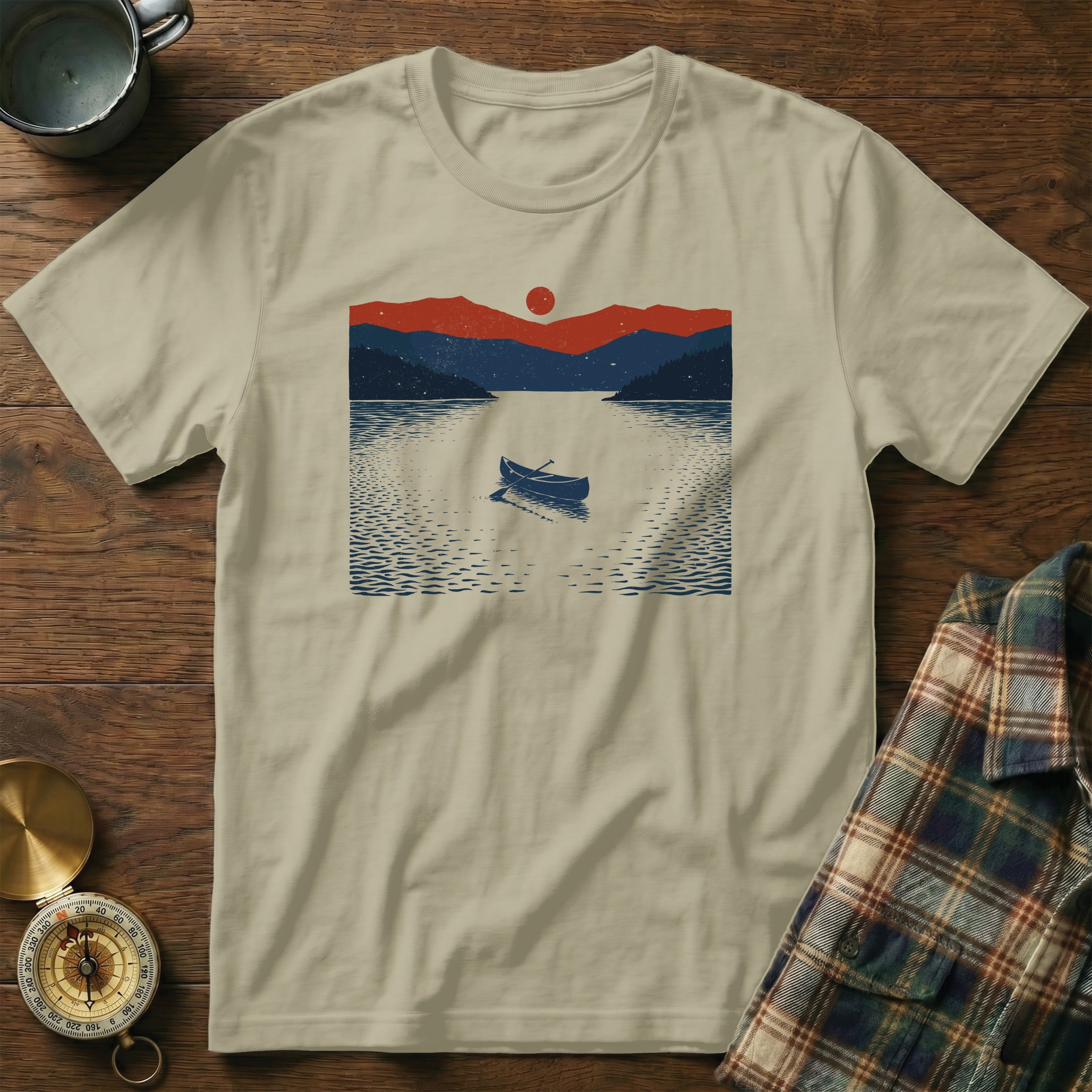 T-shirt with a graphic of a canoe on a lake at sunset with mountains.