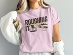 Pink t-shirt with "ROUGHING IT" text and beach scene graphic.