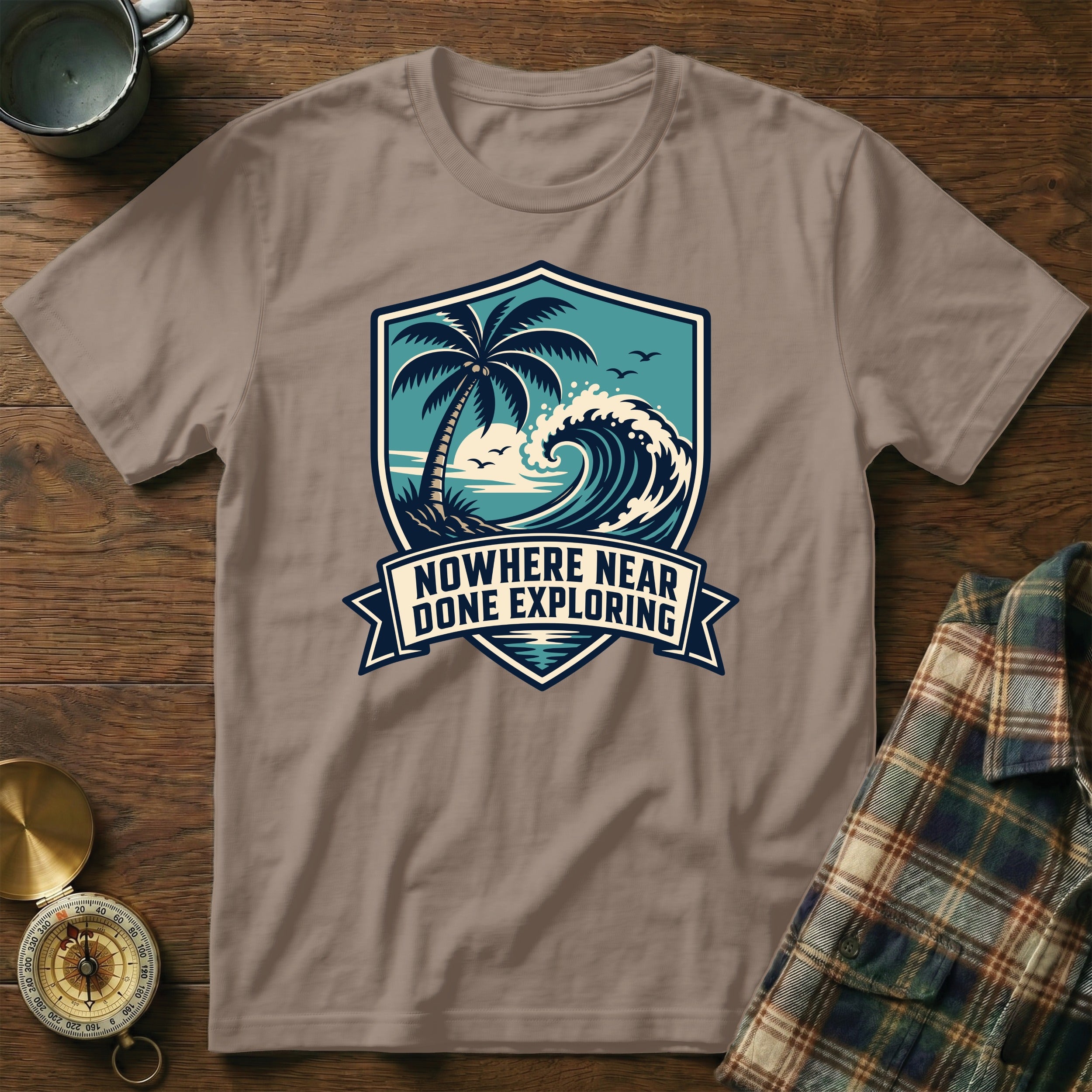 T-shirt with a shield design featuring a palm tree, wave, and the text "Nowhere Near Done Exploring."
