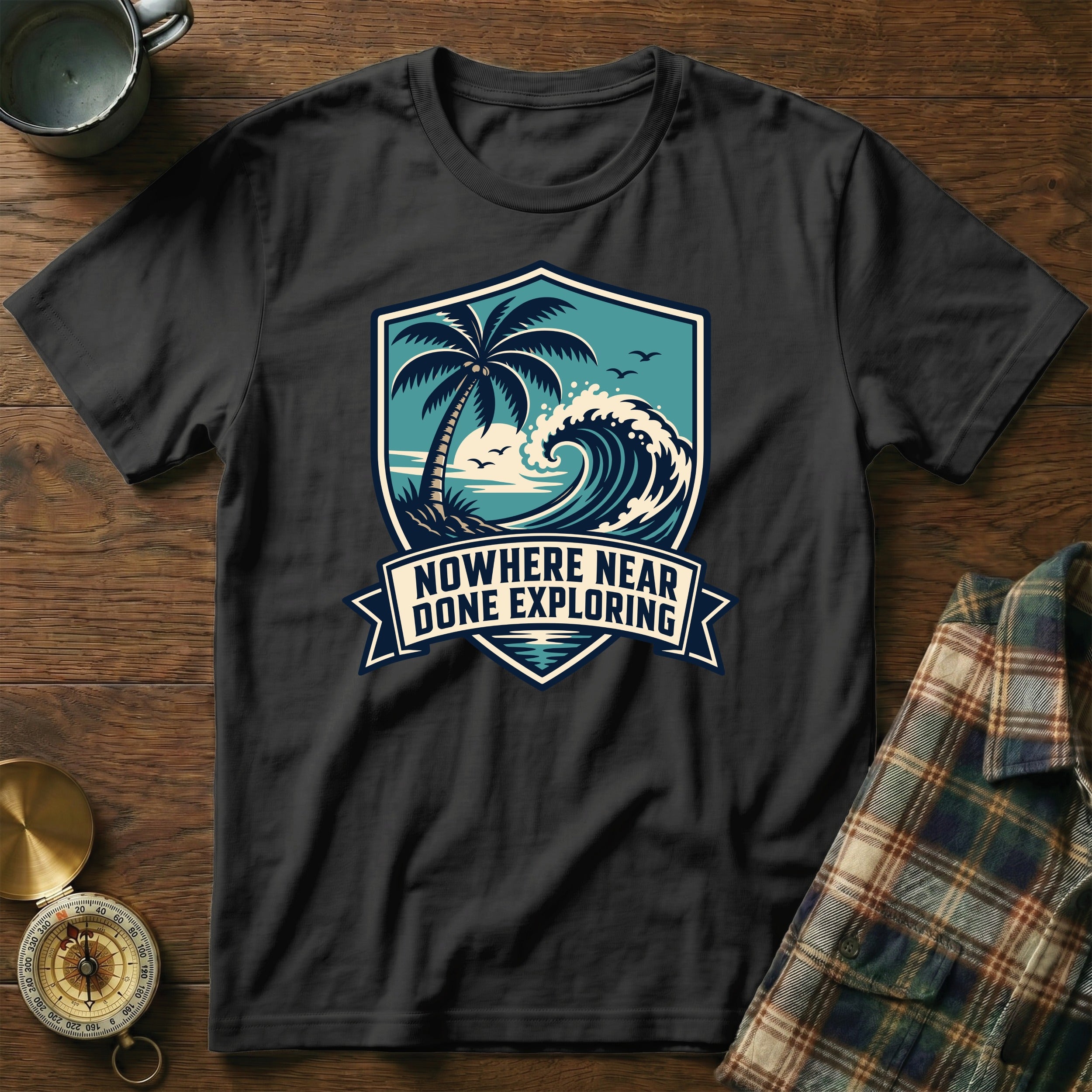 Black t-shirt with shield graphic of a palm tree, wave, and sun; text says "NOWHERE NEAR DONE EXPLORING".