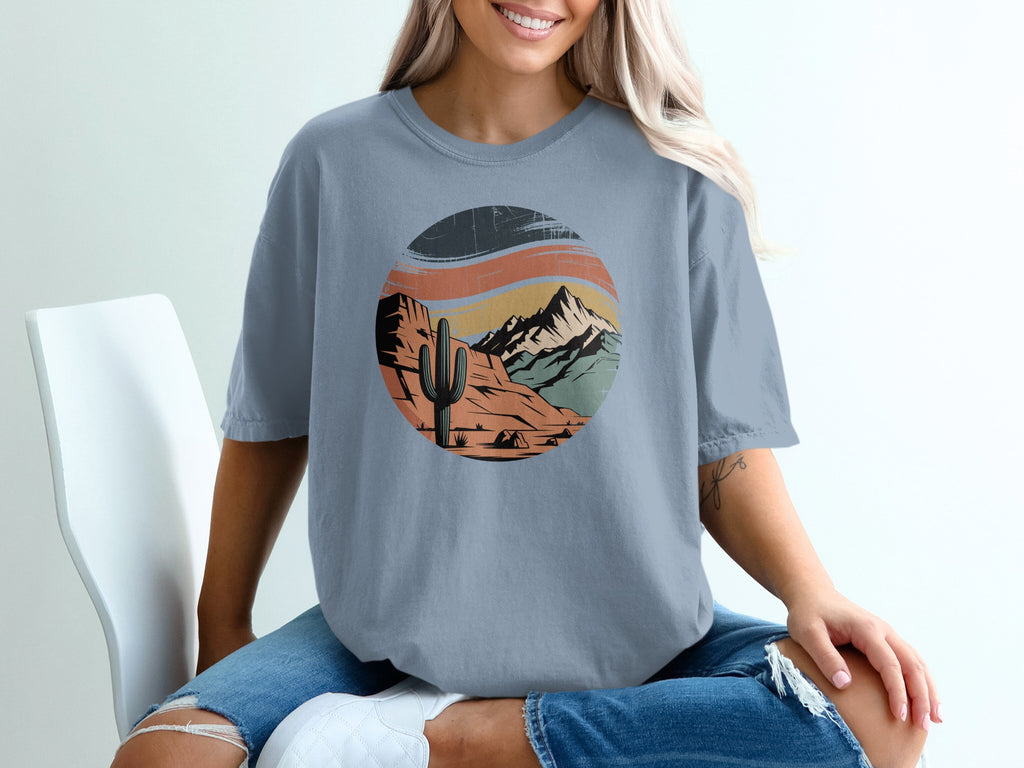 Circular desert landscape graphic with mountains, cactus, and tent on a t-shirt.