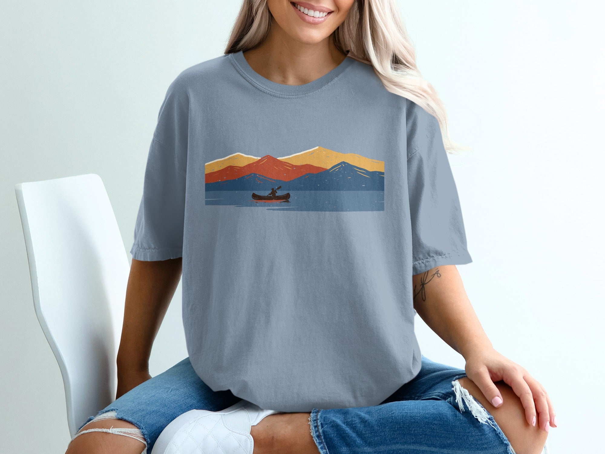 T-shirt with a graphic of a kayaker on a lake with layered mountains.