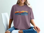 T-shirt with a minimalist, colorful mountain and lake landscape featuring a person in a canoe.