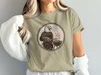 Eagle in apron grilling on a barbecue, brown graphic on a tan t-shirt.