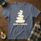 Slate blue t-shirt with stacked stones graphic and "BALANCE IS OVERRATED" text.