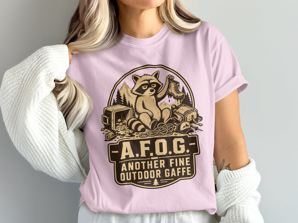 Pink t-shirt with raccoon graphic and text "A.F.O.G. ANOTHER FINE OUTDOOR GAFFE".