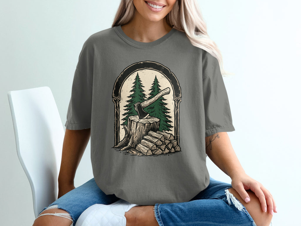 T-shirt graphic: axe in tree stump with firewood and pine trees.