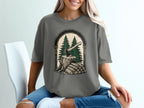 T-shirt graphic: axe in tree stump with firewood and pine trees.