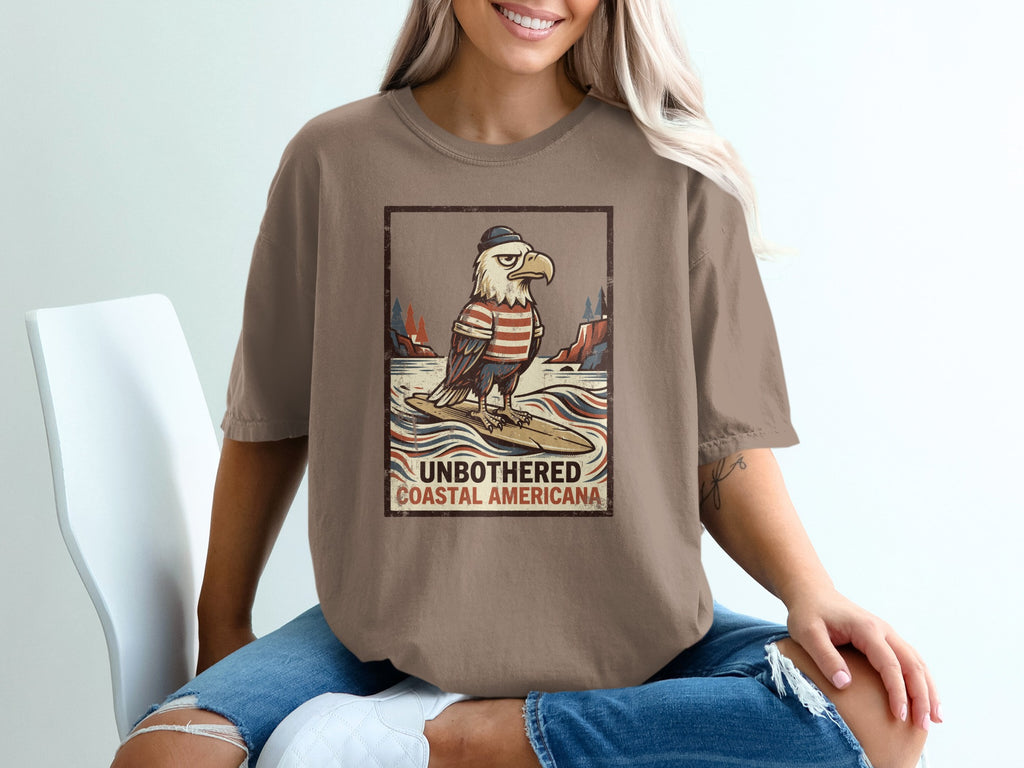 Eagle in hat and striped shirt surfing on a surfboard with "Unbothered Coastal Americana" text.