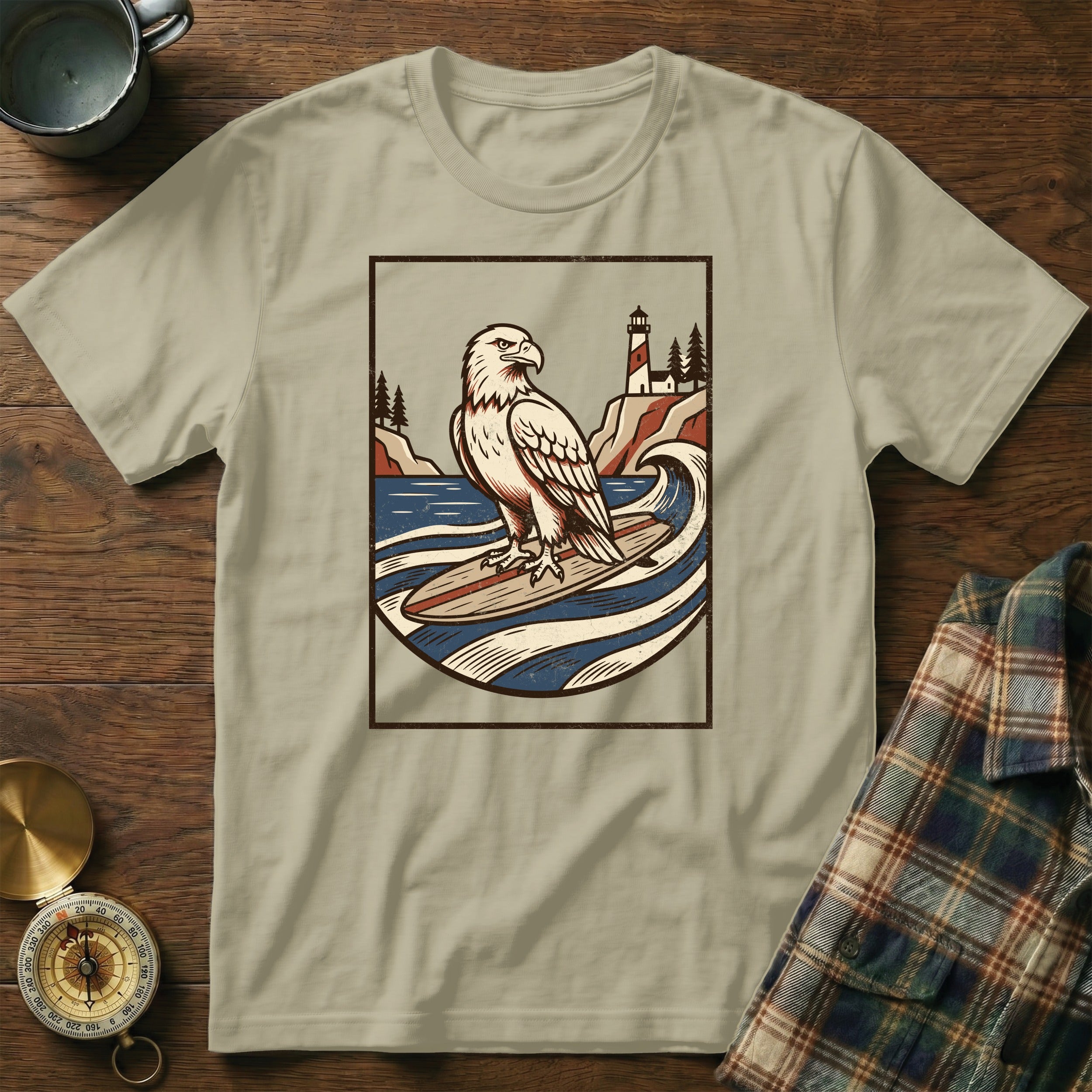 Eagle surfing on a surfboard with lighthouse and ocean graphic on t-shirt.