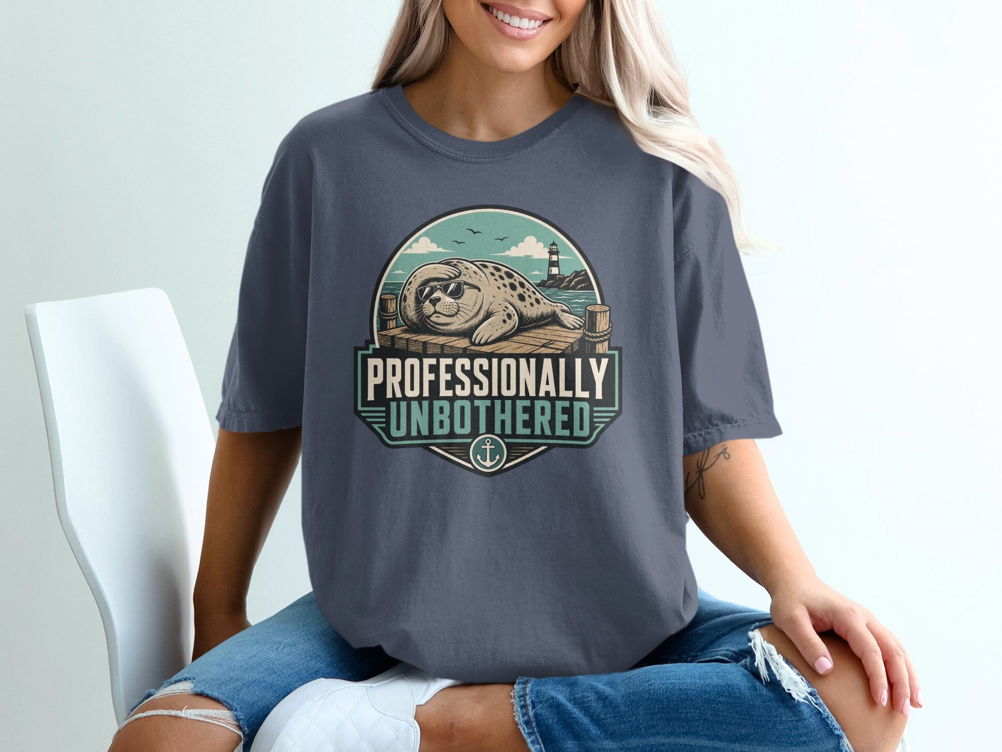 T-shirt with graphic of seal on dock, lighthouse, and text "Professionally Unbothered".