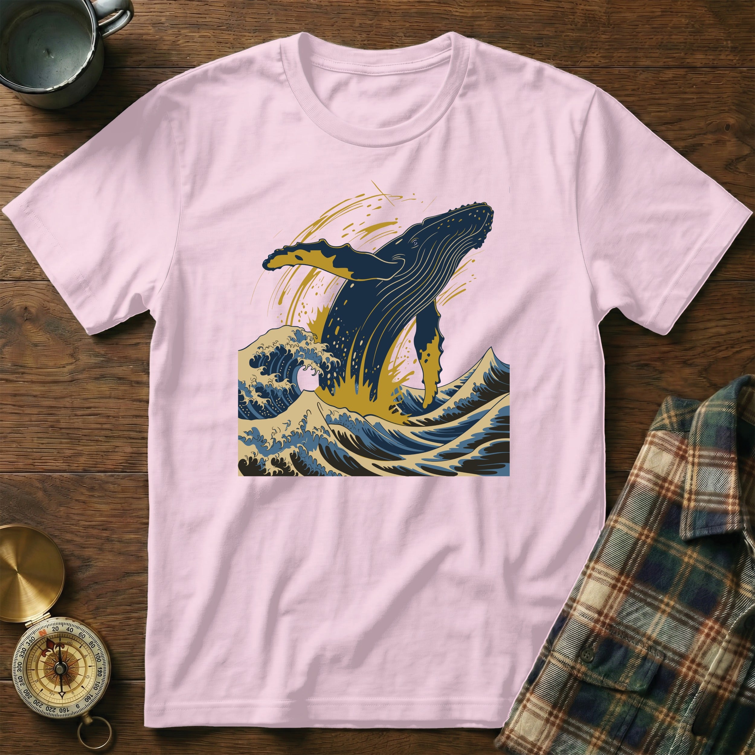 Pink t-shirt with a blue whale jumping through waves illustration.