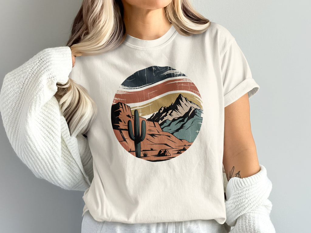 Distressed desert landscape graphic with cactus and mountains on a cream t-shirt.
