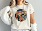 Distressed desert landscape graphic with cactus and mountains on a cream t-shirt.