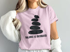 Pink t-shirt with black stacked stones graphic and "BALANCE IS OVERRATED" text.