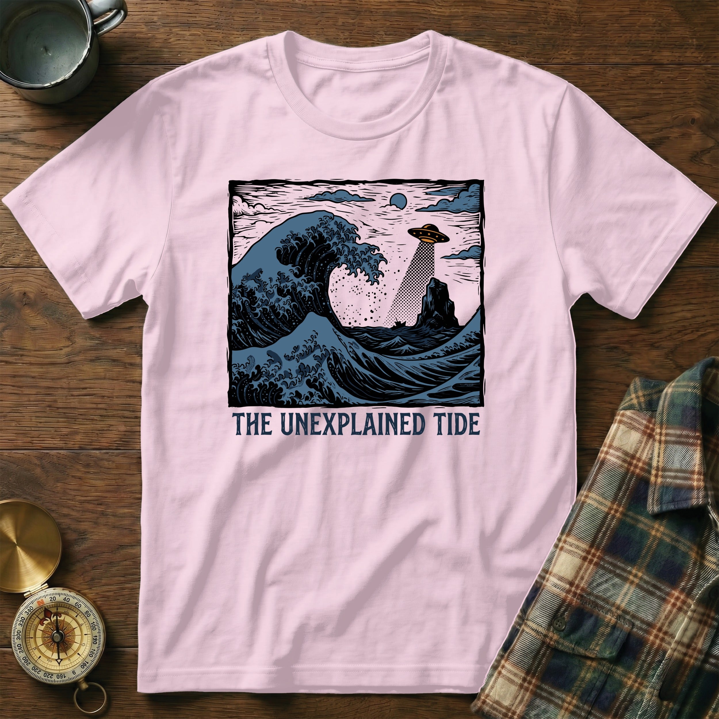 Pink t-shirt with "THE UNEXPLAINED TIDE" text and a UFO over a crashing wave.