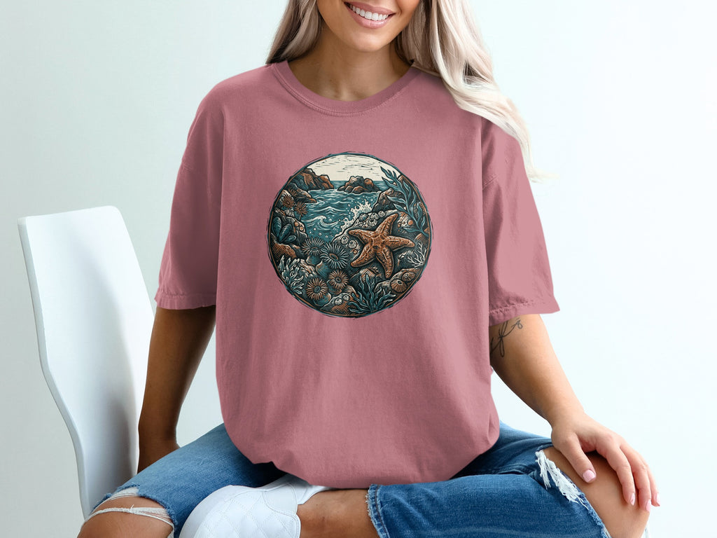 Round graphic of a starfish and seabed scene on a dusty rose t-shirt.